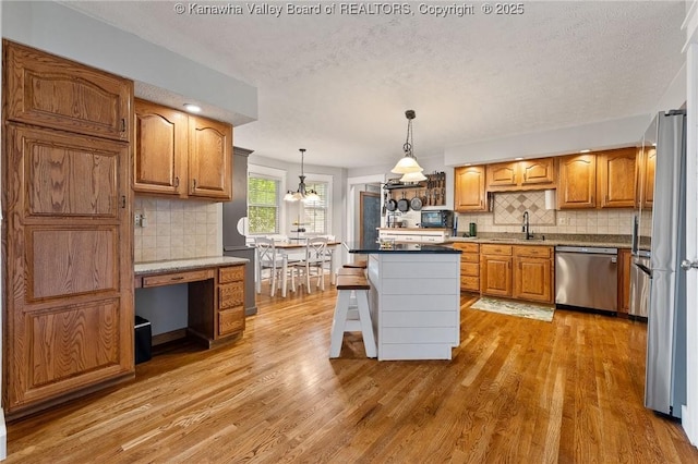 kitchen featuring stainless steel appliances, a sink, decorative backsplash, light wood finished floors, and a textured ceiling