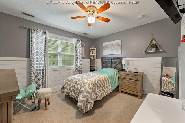 bedroom featuring carpet floors, wainscoting, a textured ceiling, a ceiling fan, and wooden walls