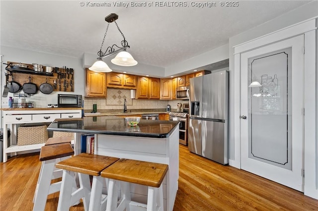 kitchen featuring appliances with stainless steel finishes, light wood-type flooring, tasteful backsplash, decorative light fixtures, and a sink