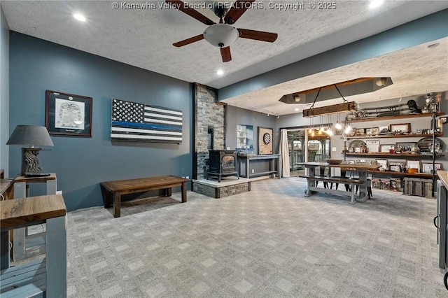 living area featuring a wood stove, carpet floors, a ceiling fan, a textured ceiling, and recessed lighting