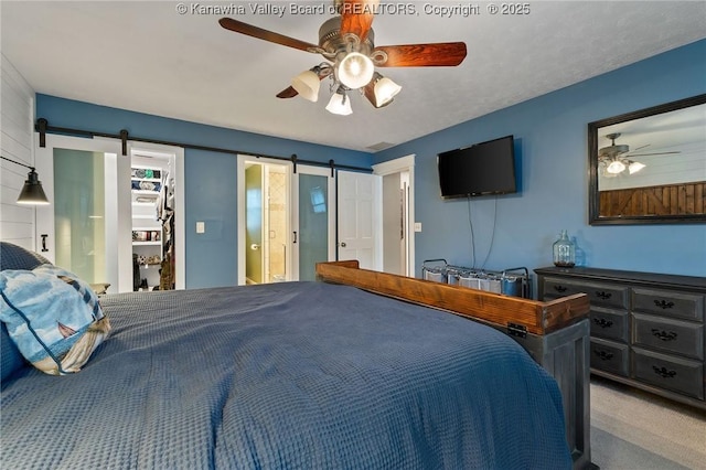 carpeted bedroom featuring a barn door, ceiling fan, a walk in closet, and a closet