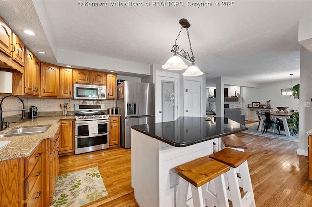 kitchen featuring appliances with stainless steel finishes, a sink, light wood-type flooring, a breakfast bar, and tasteful backsplash