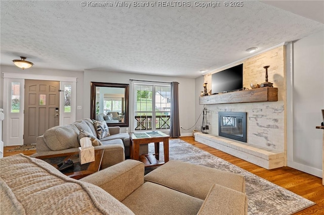 living room featuring a large fireplace, a textured ceiling, baseboards, and wood finished floors