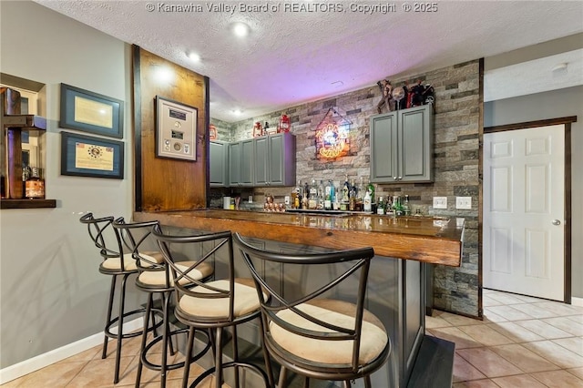 indoor wet bar featuring light tile patterned flooring, a textured ceiling, and baseboards