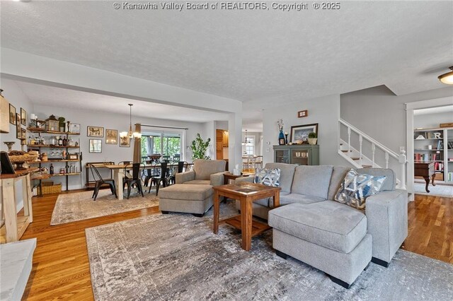 living area featuring light wood-style floors, stairs, a textured ceiling, and a chandelier