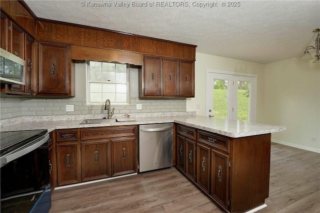 kitchen featuring appliances with stainless steel finishes, a peninsula, a sink, a textured ceiling, and tasteful backsplash
