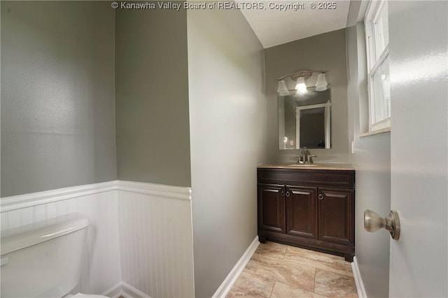 half bathroom featuring toilet, vanity, baseboards, and a wainscoted wall
