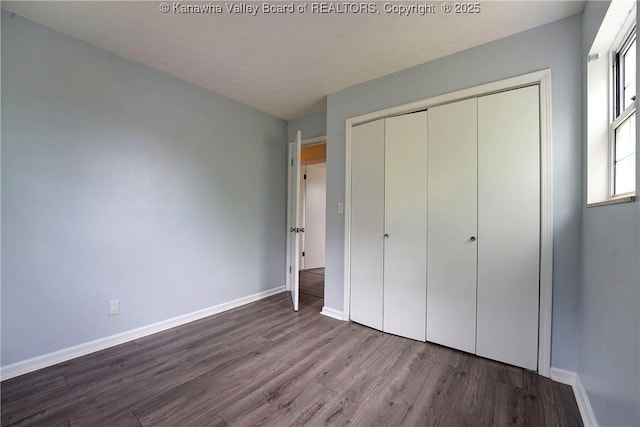 unfurnished bedroom featuring wood finished floors, baseboards, and a closet
