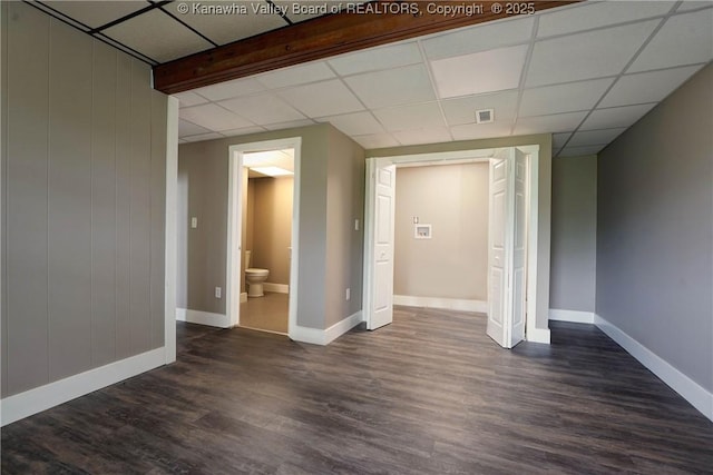 below grade area with dark wood-style flooring, baseboards, and a drop ceiling