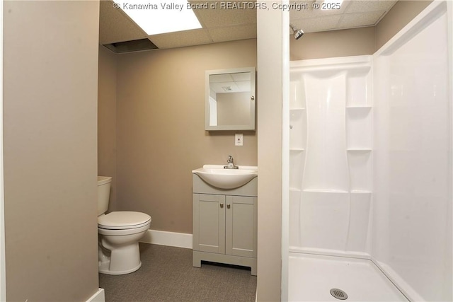 bathroom featuring a paneled ceiling, toilet, a shower stall, vanity, and baseboards