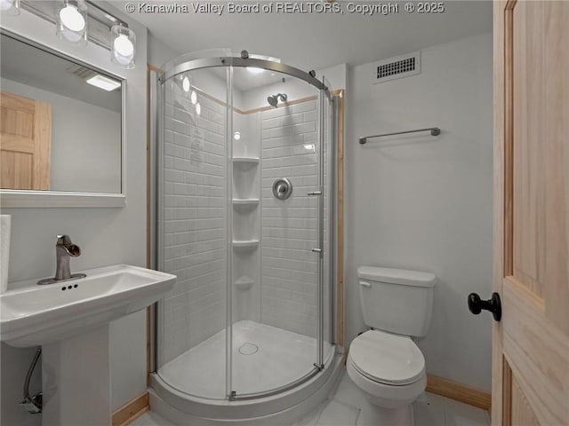 bathroom featuring toilet, a stall shower, baseboards, tile patterned floors, and a sink