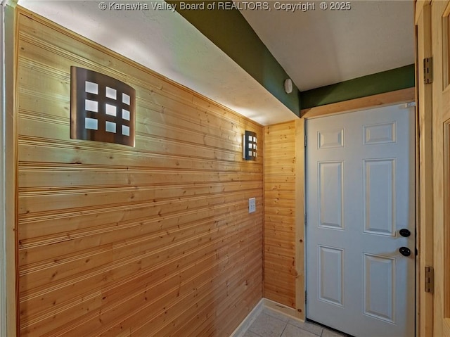 doorway with light tile patterned floors and wood walls