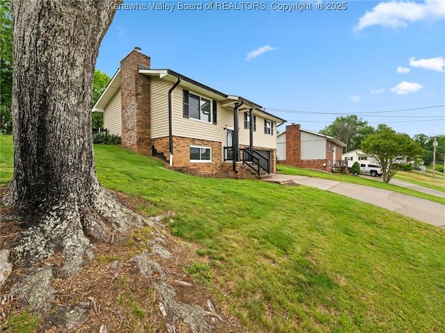 split foyer home featuring a chimney, driveway, brick siding, and a front lawn