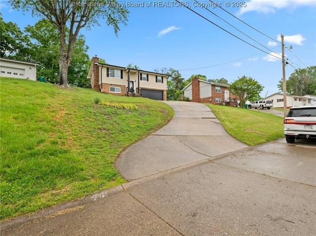 split foyer home featuring a chimney, a front lawn, driveway, brick siding, and a garage