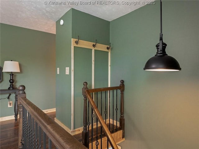 corridor featuring an upstairs landing, wood finished floors, baseboards, and a textured ceiling