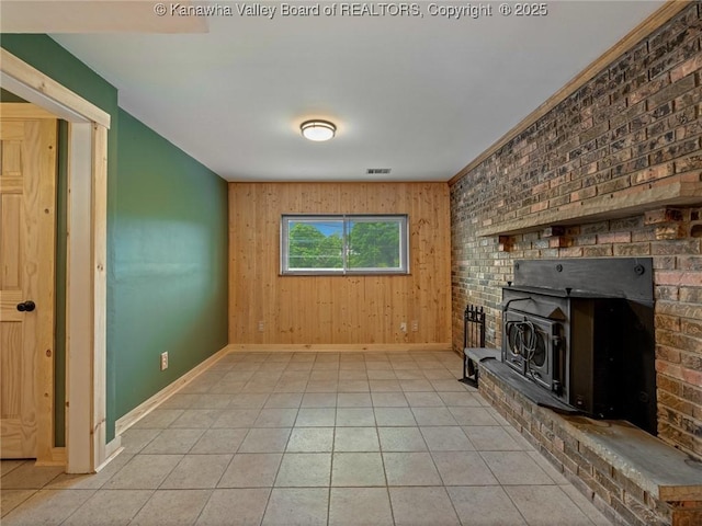 unfurnished living room with baseboards, wooden walls, light tile patterned floors, and a wood stove