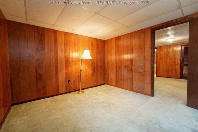 carpeted spare room with wood walls and a paneled ceiling