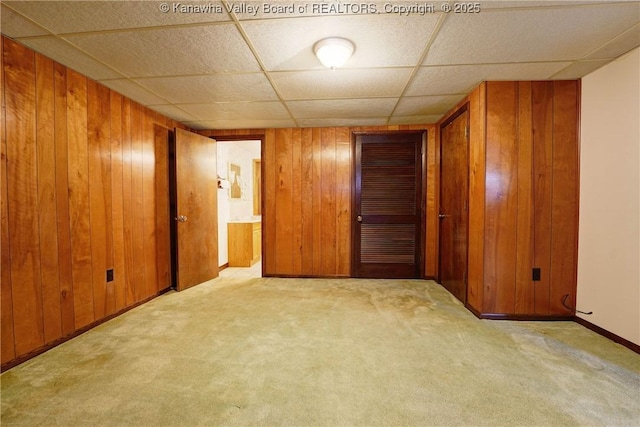 unfurnished room featuring wooden walls, a paneled ceiling, carpet, and baseboards