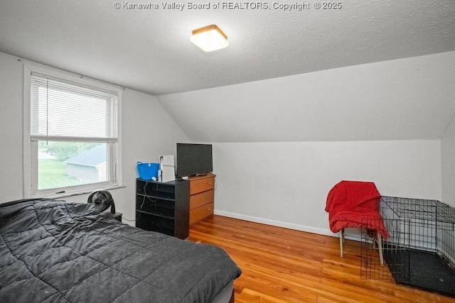 bedroom featuring wood finished floors, lofted ceiling, baseboards, and a textured ceiling