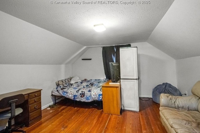bedroom with wood finished floors, vaulted ceiling, a textured ceiling, baseboards, and a desk