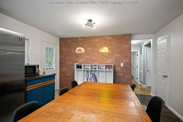 dining area with brick wall, a textured ceiling, and wood finished floors