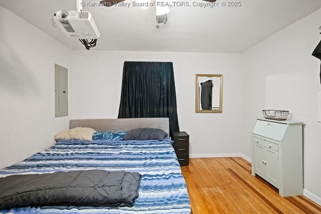 bedroom featuring light wood-style floors, baseboards, and electric panel