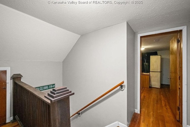 staircase featuring wood finished floors, a textured ceiling, baseboards, and vaulted ceiling