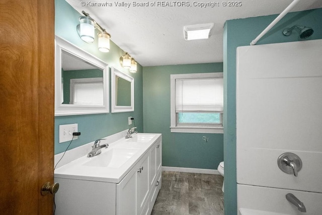 bathroom with wood finished floors, a shower, baseboards, toilet, and double vanity