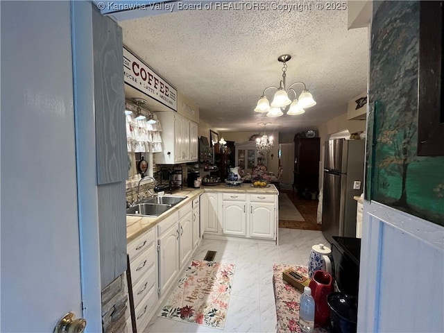 103 Chestnut Dr, Peytona, WV 25154 - kitchen featuring a sink, a chandelier, freestanding refrigerator, a textured ceiling, and white cabinets