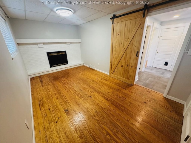 930 Mathews Ave, Charleston, WV 25302 - unfurnished living room featuring a brick fireplace, a barn door, a drop ceiling, wood finished floors, and baseboards