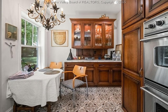 606 Fort Hill Dr, Charleston, WV 25314 - kitchen with a chandelier, light countertops, glass insert cabinets, brown cabinets, and light tile patterned flooring