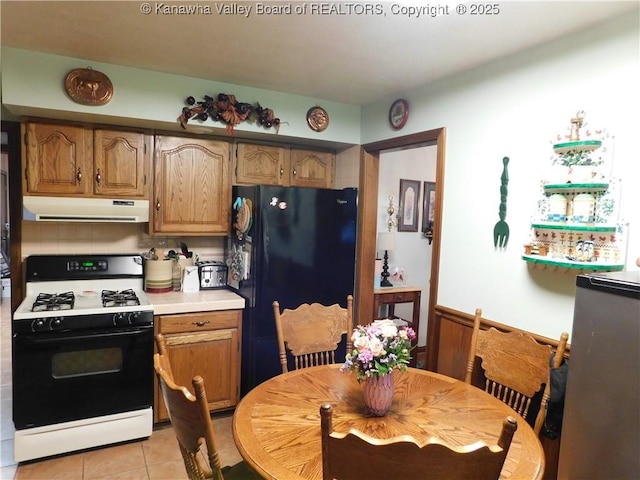 kitchen featuring gas range oven, exhaust hood, freestanding refrigerator, light countertops, and light tile patterned floors