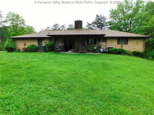 rear view of property with a chimney, a yard, brick siding, and a patio