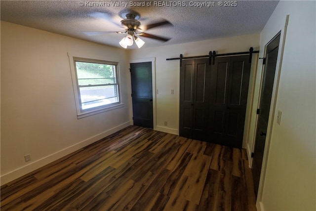 352 Hidden Valley Rd, Chapmanville, WV 25508 - unfurnished bedroom featuring dark wood-type flooring, a textured ceiling, a barn door, baseboards, and a ceiling fan