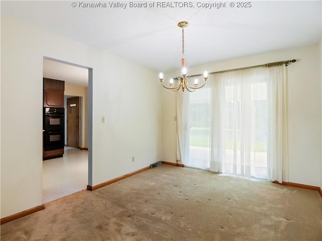 spare room featuring light colored carpet, a chandelier, and baseboards