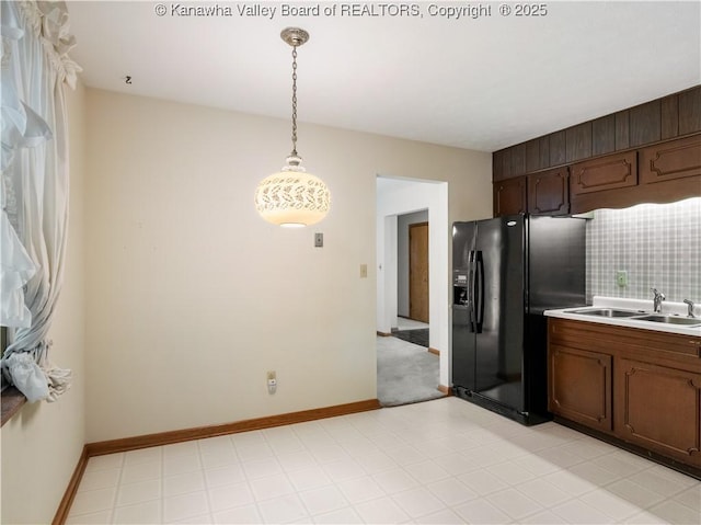 kitchen featuring black fridge with ice dispenser, a sink, hanging light fixtures, light countertops, and baseboards
