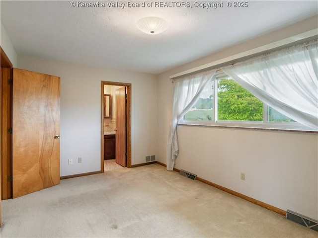 unfurnished bedroom with light colored carpet, baseboards, and ensuite bathroom