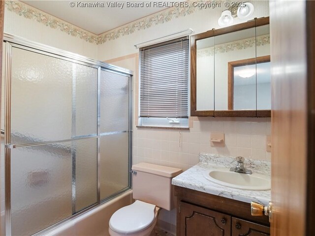full bathroom featuring tile walls, vanity, enclosed tub / shower combo, toilet, and tasteful backsplash