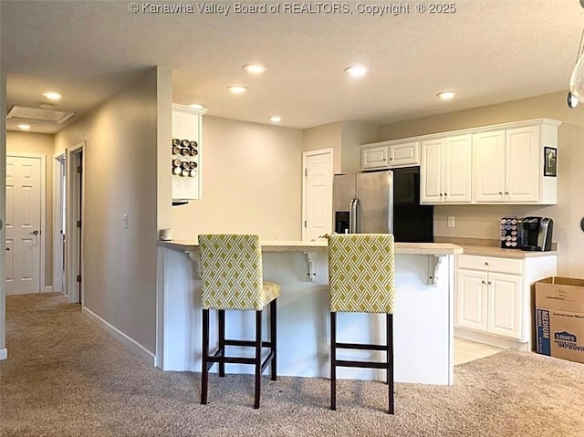 kitchen with stainless steel refrigerator with ice dispenser, light carpet, a breakfast bar, a peninsula, and white cabinetry