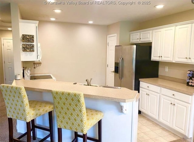 kitchen with a peninsula, a breakfast bar area, a sink, white cabinetry, and light countertops
