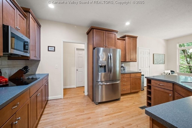 16 Pinnacle Dr, Charleston, WV 25311 - kitchen with appliances with stainless steel finishes, dark countertops, light wood-type flooring, tasteful backsplash, and brown cabinets