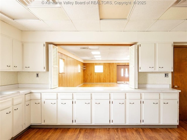 463 Gap View Dr, Charleston, WV 25326 - kitchen with a paneled ceiling, light countertops, white cabinets, light wood-style flooring, and wood walls