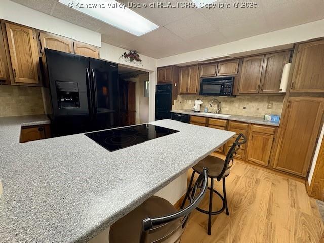2011 Archibald Dr, Charleston, WV 25320 - kitchen with black appliances, a kitchen breakfast bar, a sink, light wood-style flooring, and light countertops