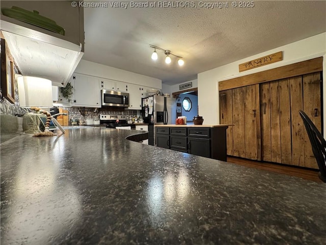 3902 Poca River Rd S, Poca, WV 25159 - kitchen with stainless steel appliances, white cabinetry, dark countertops, decorative backsplash, and a peninsula