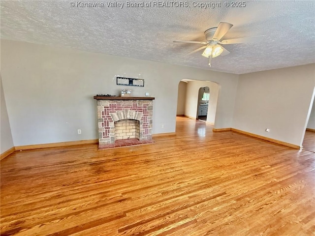 300 Sycamore St, Ravenswood, WV 26164 - unfurnished living room featuring a textured ceiling, wood finished floors, a ceiling fan, arched walkways, and a stone fireplace