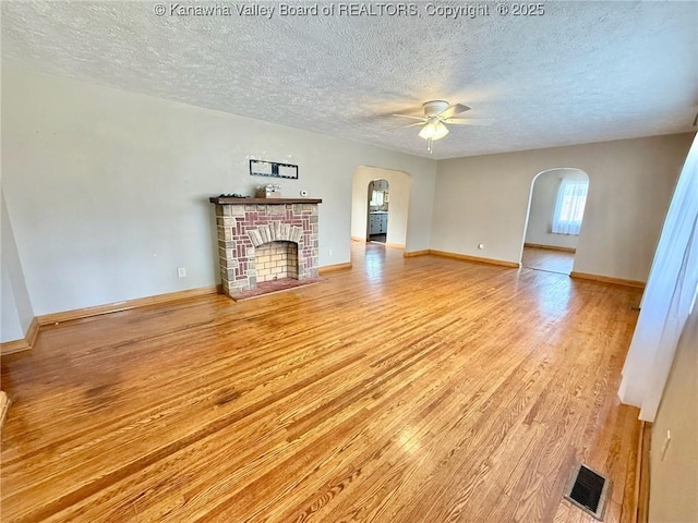 300 Sycamore St, Ravenswood, WV 26164 - unfurnished living room with arched walkways, light wood-style flooring, a textured ceiling, ceiling fan, and a brick fireplace