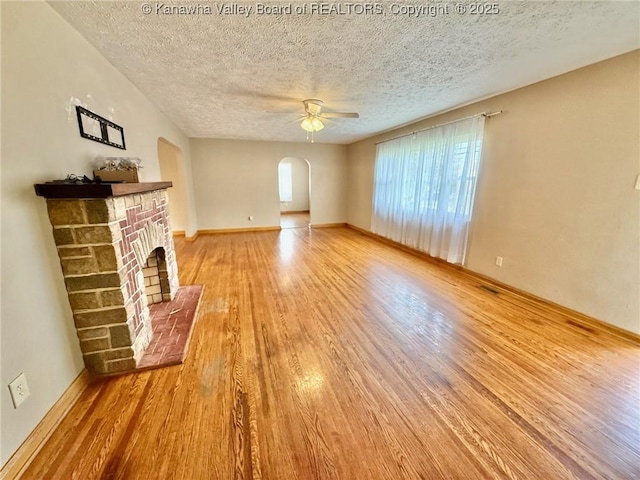 300 Sycamore St, Ravenswood, WV 26164 - unfurnished living room with wood finished floors, a fireplace, ceiling fan, a textured ceiling, and arched walkways