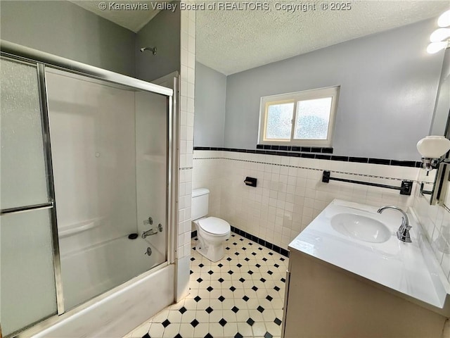 300 Sycamore St, Ravenswood, WV 26164 - bathroom with toilet, vanity, bath / shower combo with glass door, a wainscoted wall, and tile walls