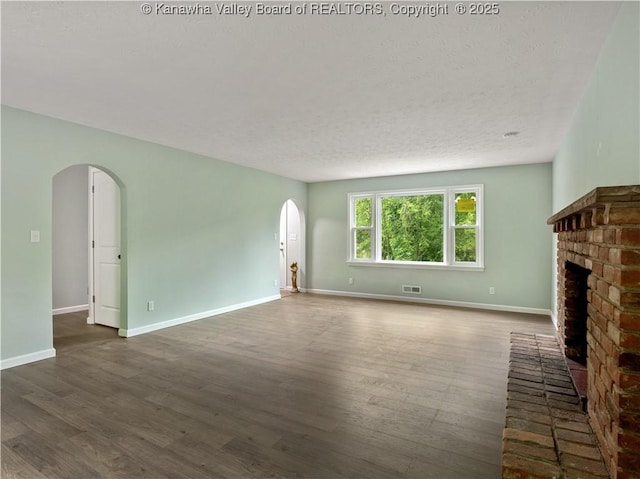 1255 Park Ave, Charleston, WV 25302 - unfurnished living room with arched walkways, dark wood-type flooring, a brick fireplace, a textured ceiling, and baseboards
