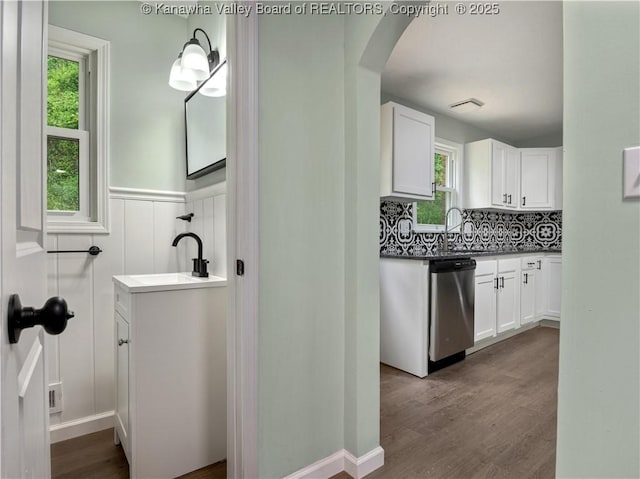 1255 Park Ave, Charleston, WV 25302 - kitchen with stainless steel dishwasher, arched walkways, white cabinets, dark wood-style floors, and a wainscoted wall